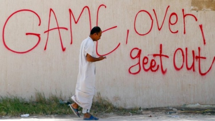 Мъж минава покрай надпис "Край на играта" в Адждабия. Снимка: Reuters