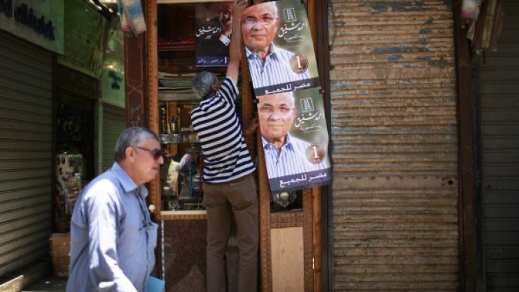 Мъж окачва плакат на кандидата за президент Ахмед Шафик на магазин в Кайро. Снимка: Reuters