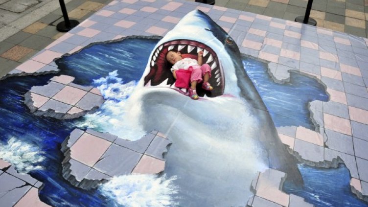 Китайче се излегнало между челюстите на нарисувана в 3D формат акула. Снимка: Reuters