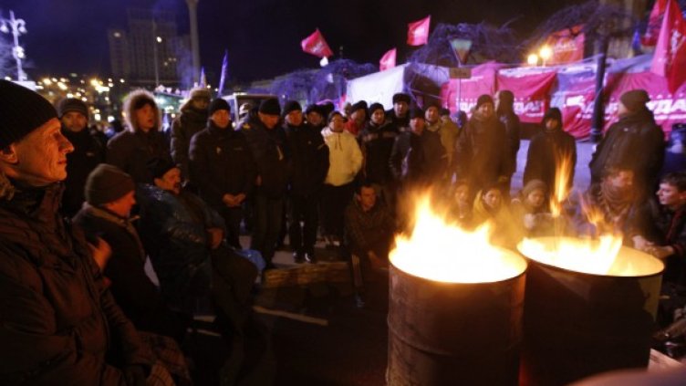 Митингуващи се греят край огън, запален в големи варели. Снимка: Ройтерс