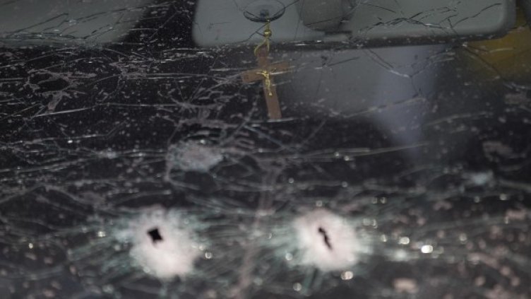 Кръст се вижда зад стъкло на кола, надупчена от куршуми при сблъсъците. Снимка: Ройтерс