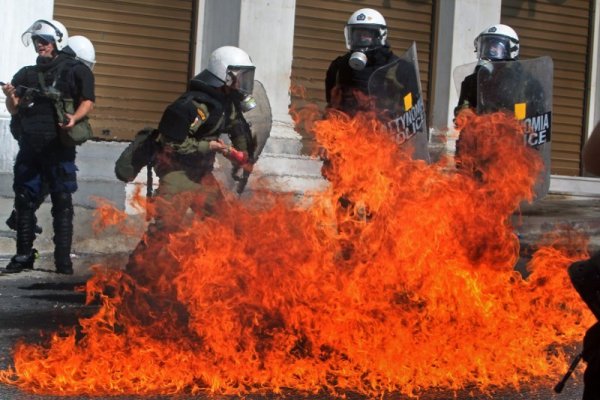 Полицаи се пазят, след като са замеряни с коктейли Молотов, по време на поредния ден на протести в гръцката столица Атина. Снимка: БТА