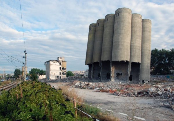 От сградите и съоръженията на територията на бившото предприятие &quot;Зърнени храни&quot; в Благоевград продължават все още да стърчат наклонени към вътрешния двор 12-те силоза, месец след опита да бъдат съборени чрез взривяване. Продължават и опитите високите около 35 метра съоръжения да бъдат срутени, за да се разчисти теренът. Снимка: БТА