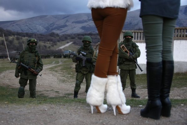 Жени наблюдават военни, за които се смята, че са руснаци, които се групират до украинската военна база в Перевалное. Снимка: Reuters