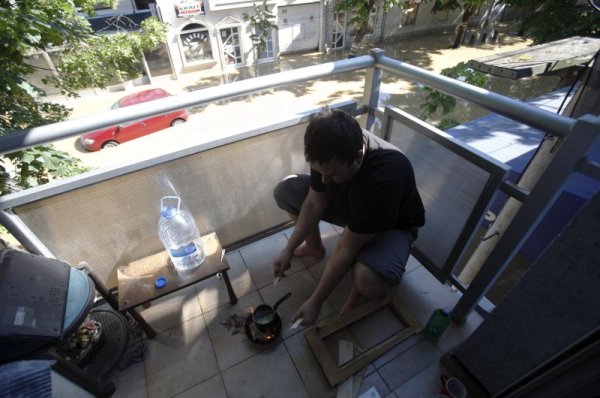 Жител си прави кафе на балкона, а улицата под него се е превърнала в река. Снимка: Reuters