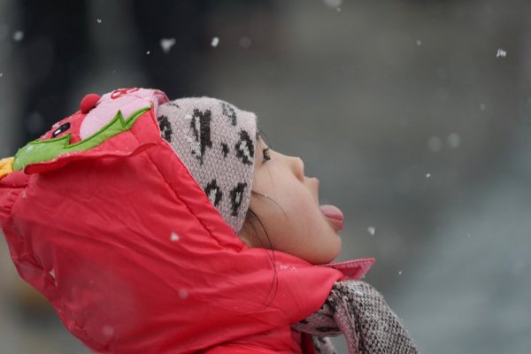 Момиченце се опитва да улови с уста снежинки от падащия сняг над парк в Пекин. Снимка: БТА
&nbsp;