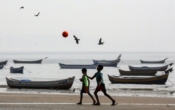 Деца си играят с топка покрай рибарски лодки в Мумбай, Индия. Снимка: БГНЕС
&nbsp;