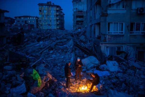 Мъже се греят на открит огън на фона на отломките от жилищна сграда в турския град Хатай след жестокото земетресение през февруари. Снимка: БГНЕС